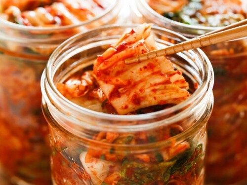 Pot met rode kimchi, met stokjes een stuk kool omhooggehouden