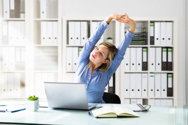 Medewerkster rekt zich uit achter haar laptop op kantoor