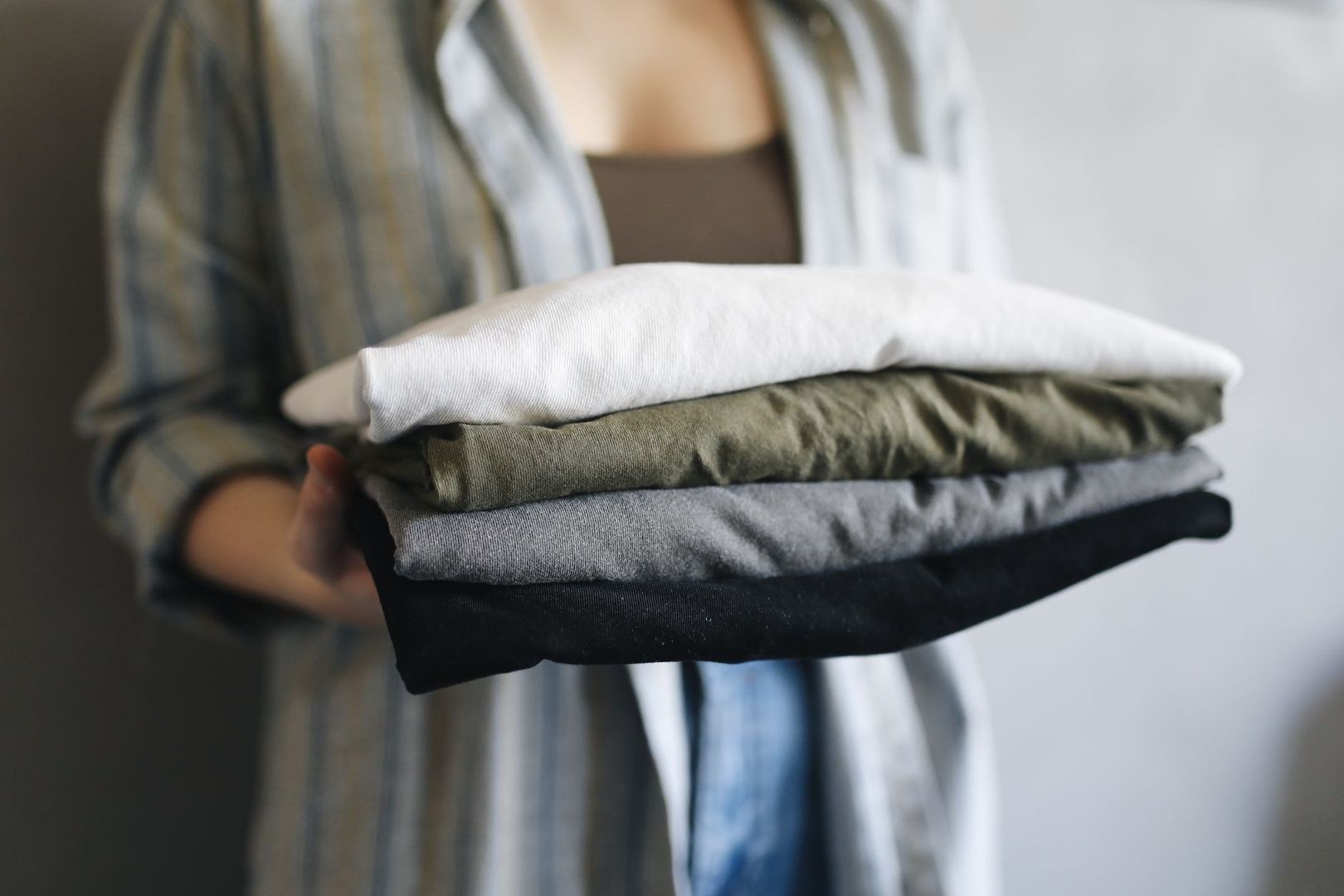 Persoon houdt een stapel opgevouwen kleding vast in natuurlijke tinten
